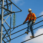 Lineman berdiri di atas kabel listrik dengan perlengkapan keselamatan.