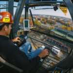 Operator crane mengendalikan alat berat dari dalam kabin di atas lokasi konstruksi.